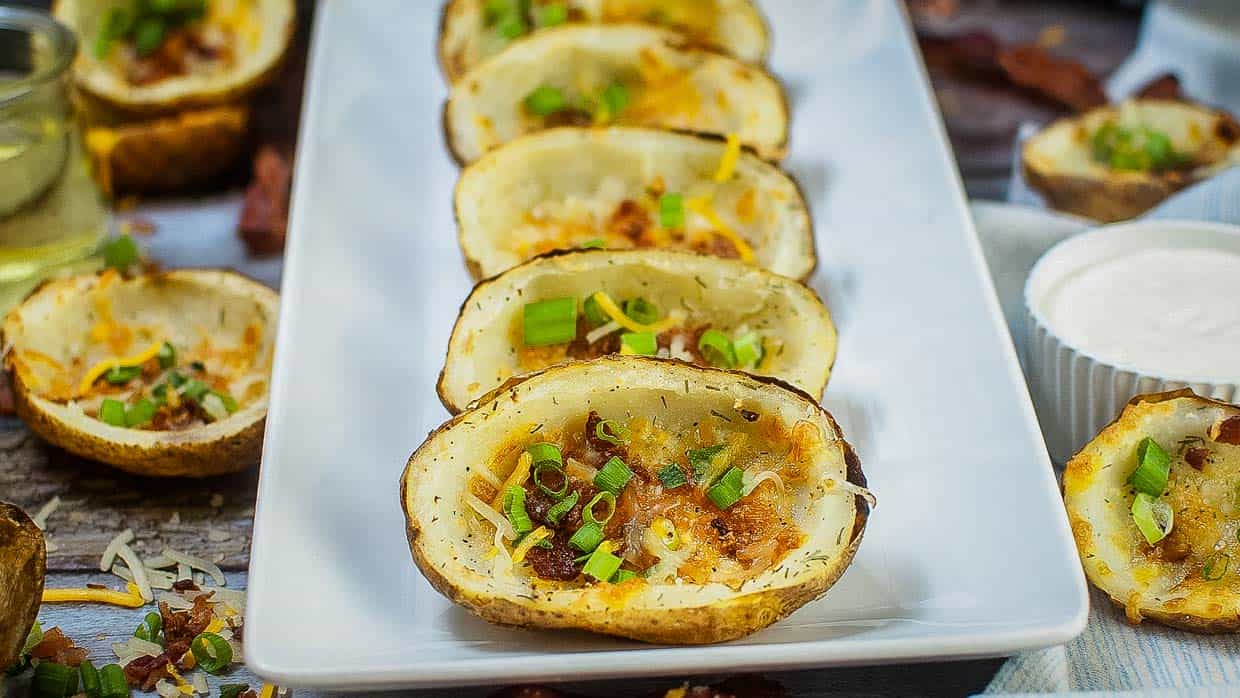 Plate of potato skins topped with cheese, bacon and chives.
