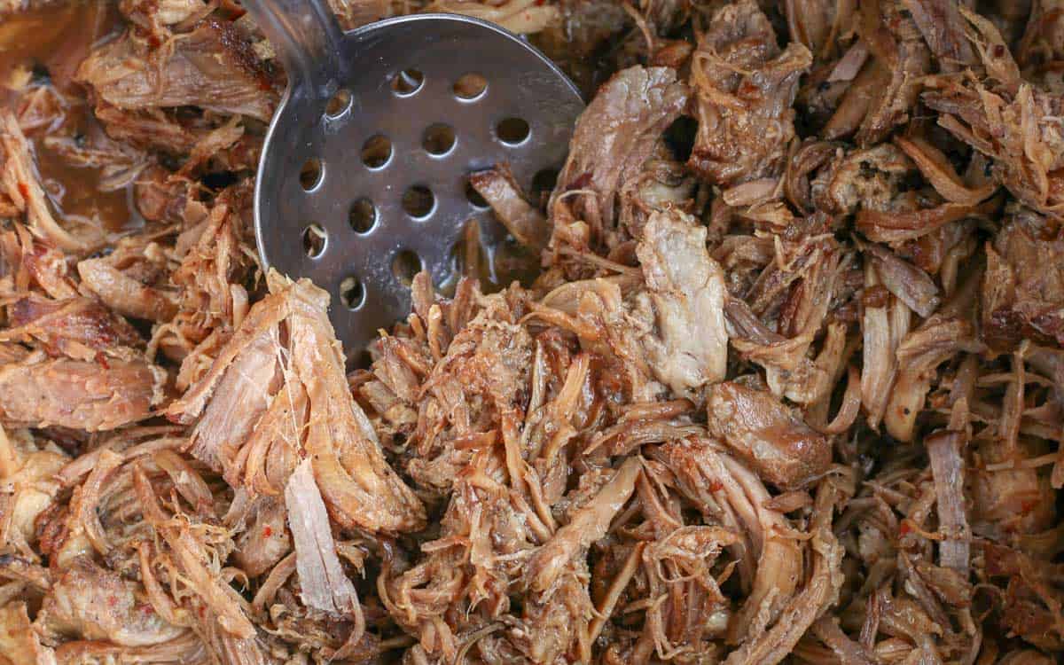 Shredded pork in an instant pot with a serving spoon.