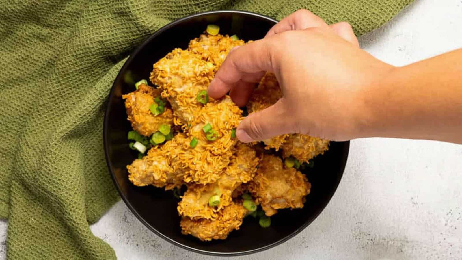 Hand reaching into a bowl of ramen fried chicken pieces.
