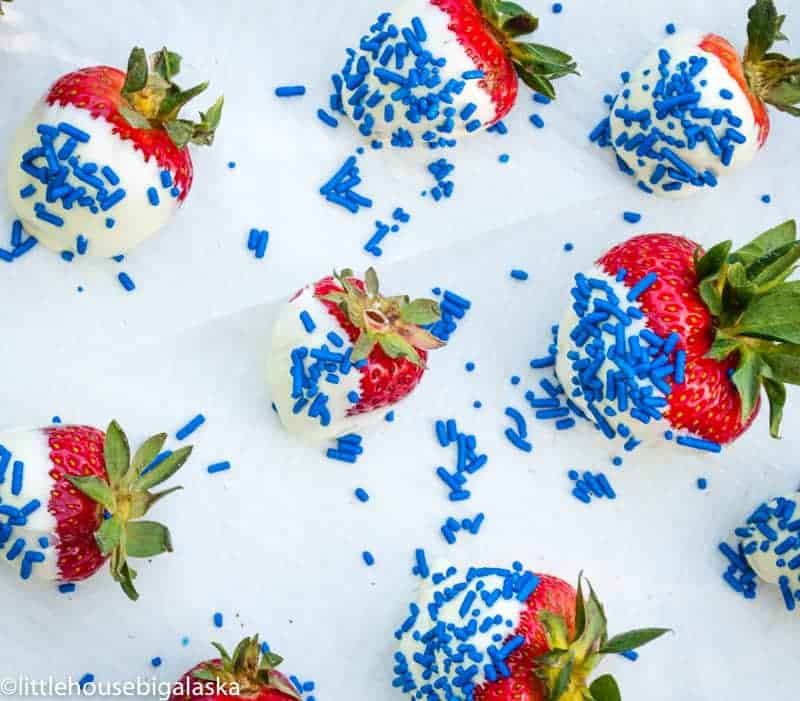 Red, white and blue strawberries on a cookie sheet lined with parchement. 