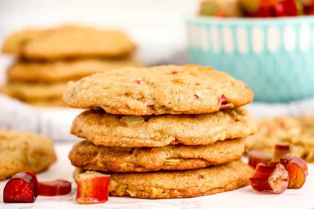4 stacked rhubarb cookies with small pieces of rhubarb and blue bowl in background