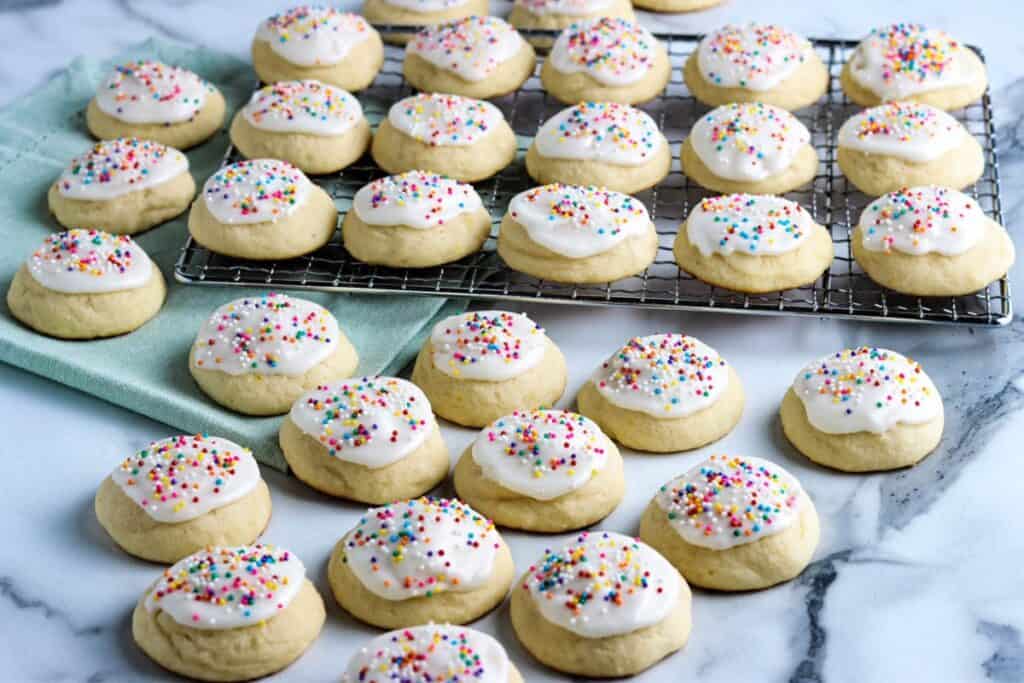 Ricotta cookies with icing and colored sprinkles on a cooling rack and on the counter.