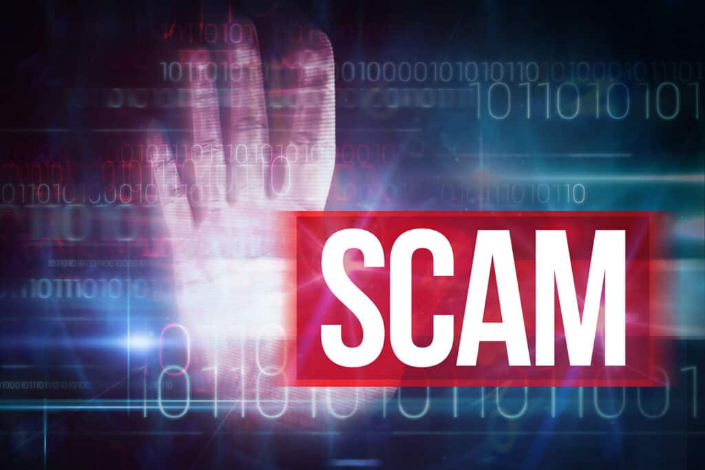 Hand with the word Scam on a computer screen.