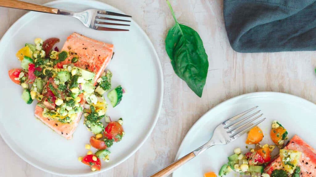 Seared salmon filets with tomato corn salsa on white plates with forks.