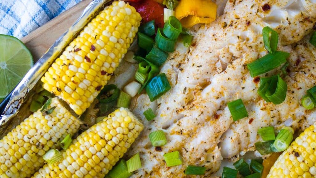 Sheet pan fish cooked with corn and veggies and topped with green onions.