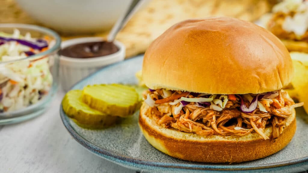 pulled chicken sandwich topped with coleslaw with pickles on the side.