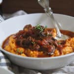 Slow cooker short rib ragu in a bowl over mashed sweet potatoes with a fork.