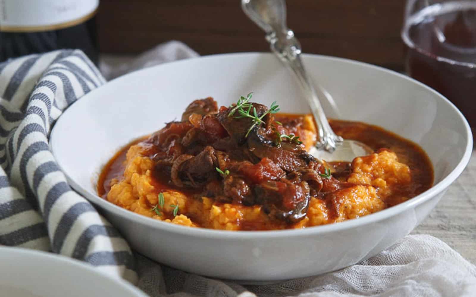 Slow cooker short rib ragu in a bowl over mashed sweet potatoes with a fork.