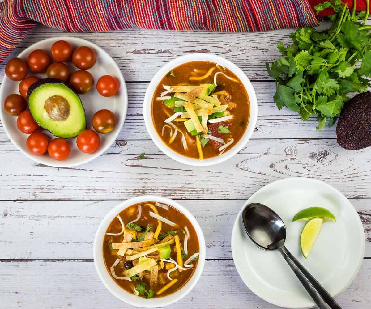 Smoked Chicken Tortilla Soup in two white bowls with garnishes nearby.