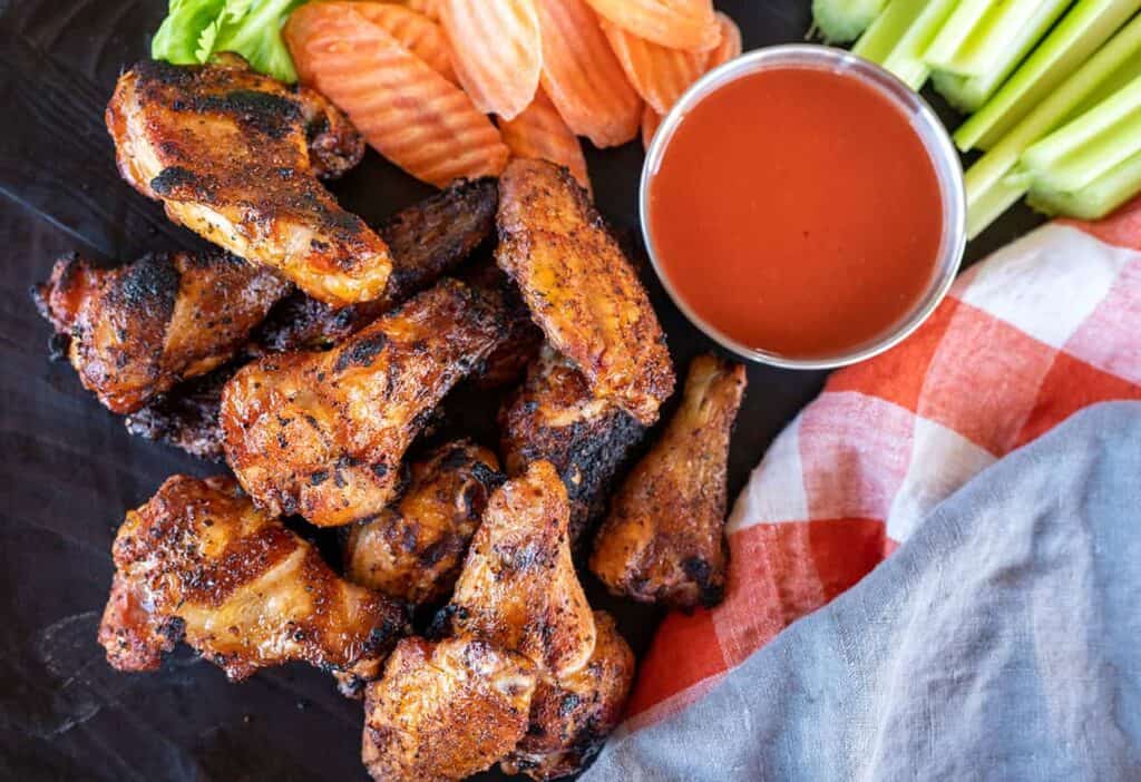 smoked chicken wings on a black plate with sauce and veggies.