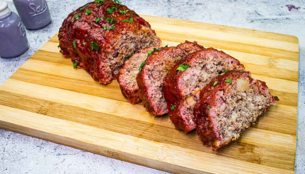 Sliced Smoked Meatloaf on a cutting board with salt and pepper shakers on the side.