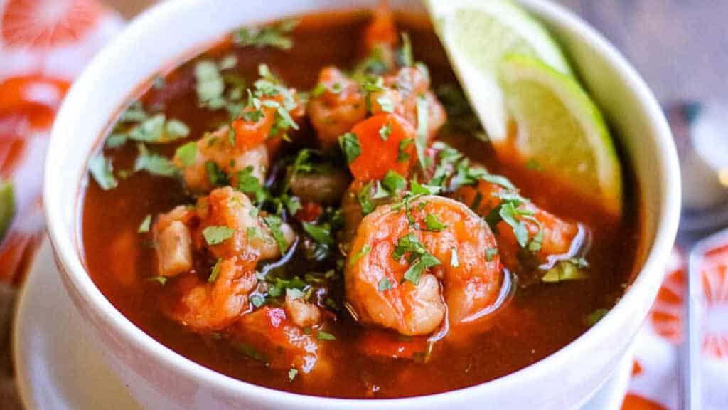 white bowl with sopa de camaron with lime wedges.