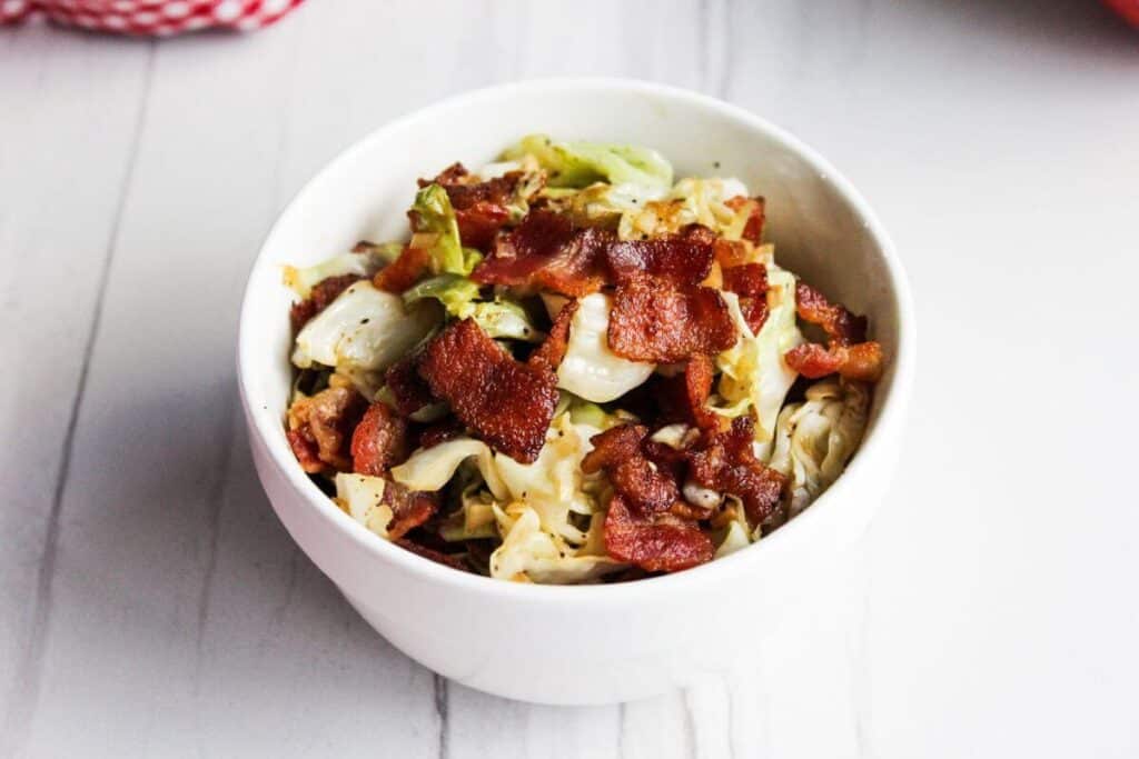 Cabbage and bacon in white serving bowl.