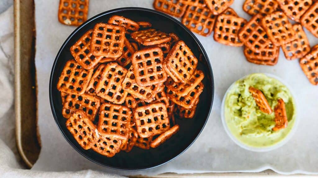 Spicy seasoned pretzels in a black bowl with small bowl of guacamole on the side.