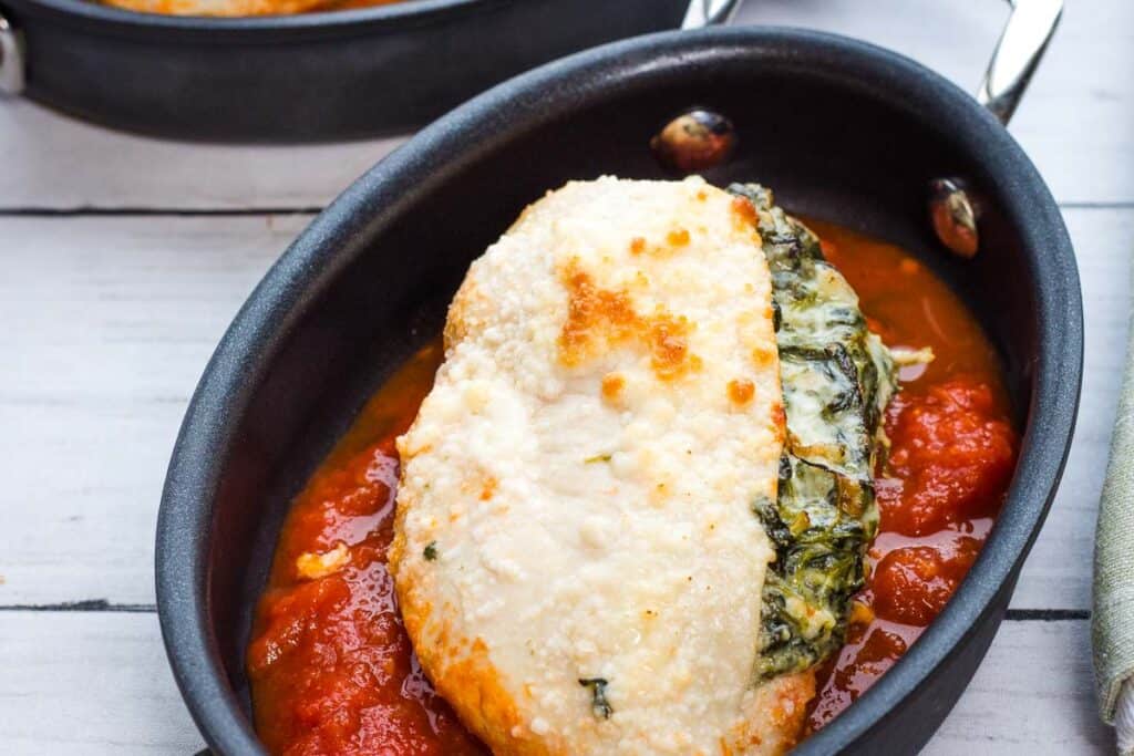 Spinach Stuffed Chicken with tomato sauce in a black oval dish.