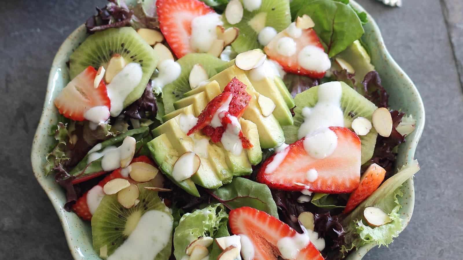 Strawberry avocado honey lime salad in a teal scalloped plate.