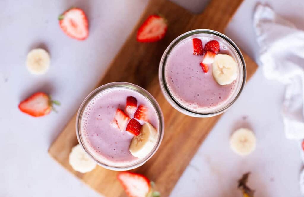 Overhead shot of two glasses of strawberry banana smoothies on a wood board.