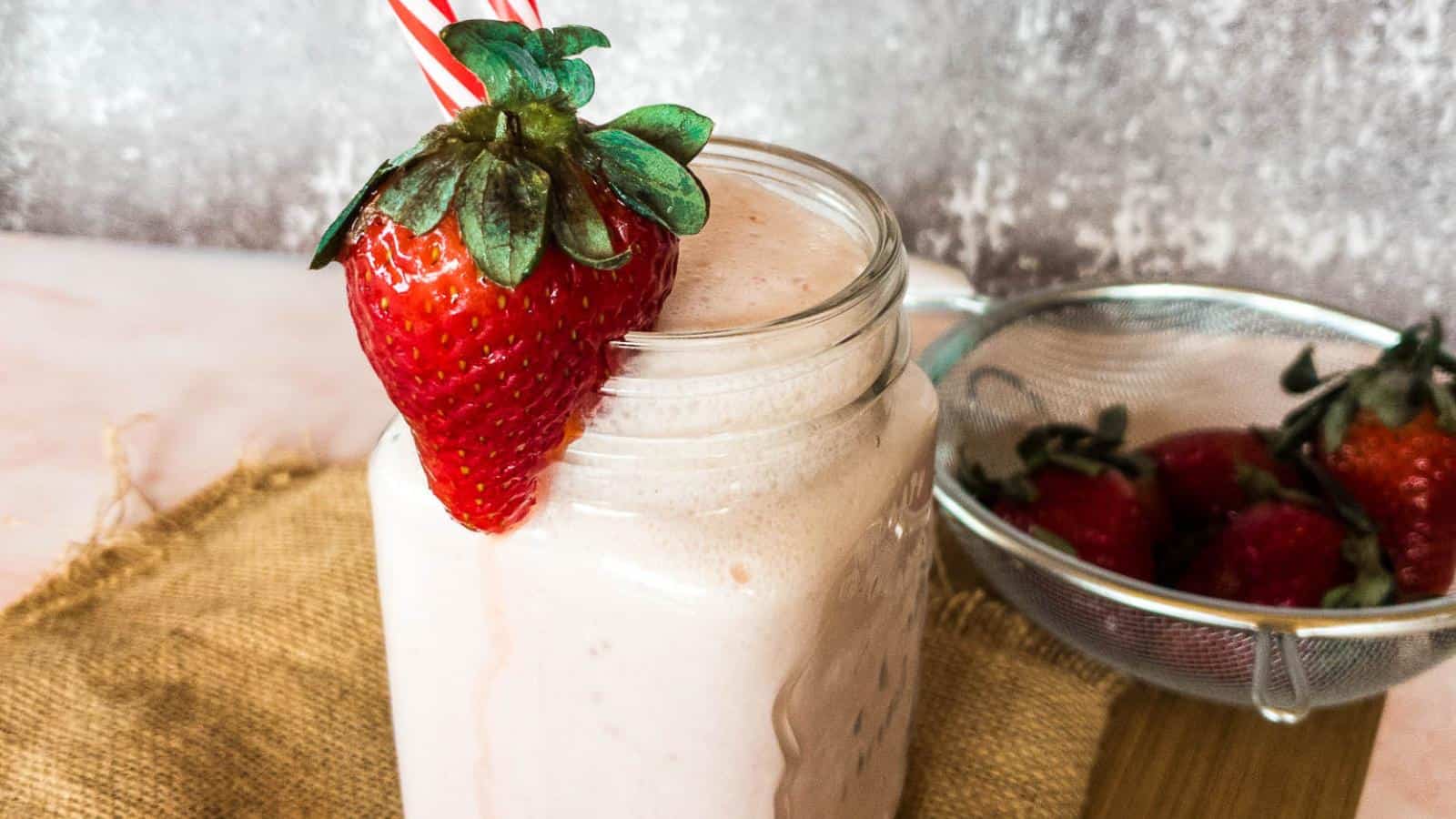 A picture of a strawberry smoothie in glass with fresh strawberry on rim.