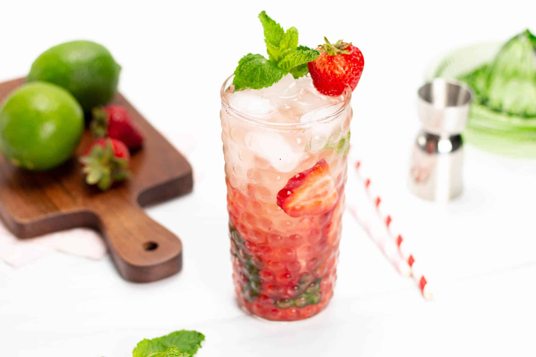 a cutting board with limes and strawberries next to a strawberry cocktail.