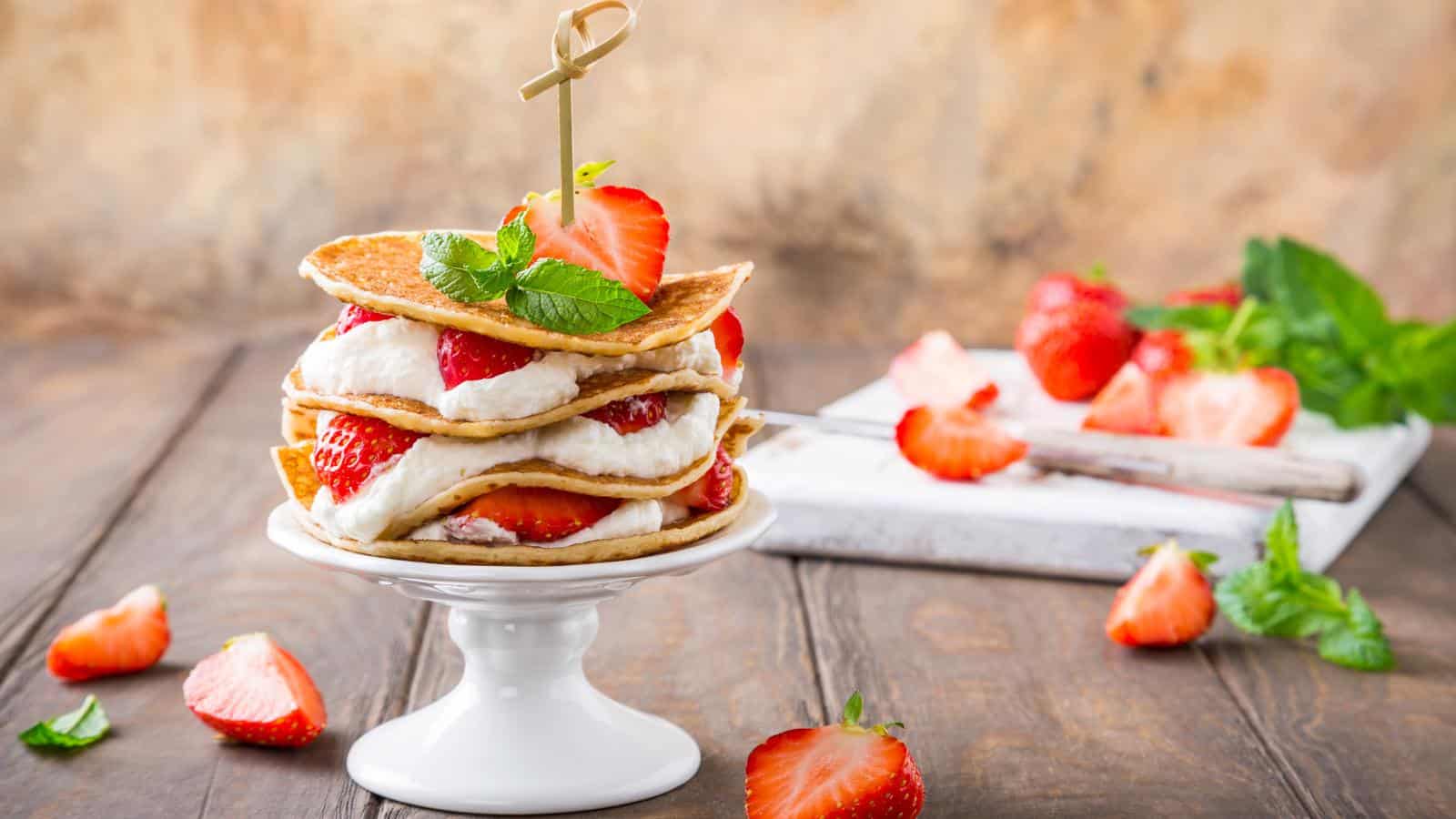 A stack of strawberry shortcake pancakes on white stand with toothpick and mint leaves.
