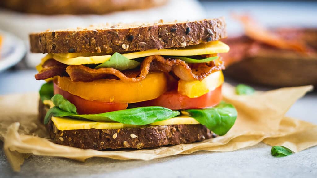 Bacon lettuce and tomato sandwich with cheese on parchment paper.