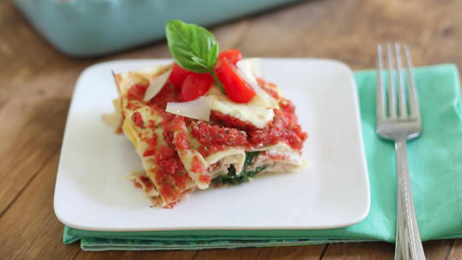 Simple summer lasagna slice on a white plate with garnish of a basil leaf.