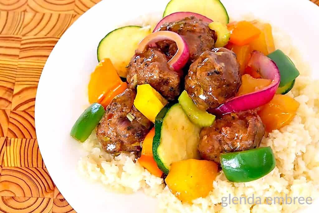 Sweet and Sour Meatballs over rice on a white plate.