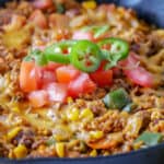 Closeup of a skillet with ground beef, cheese and tomatoes.