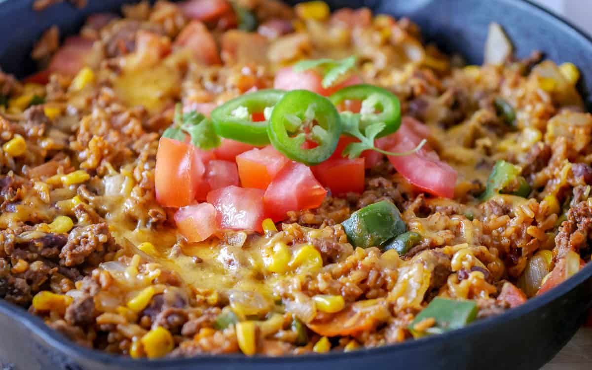 Closeup of a skillet with ground beef, cheese and tomatoes.