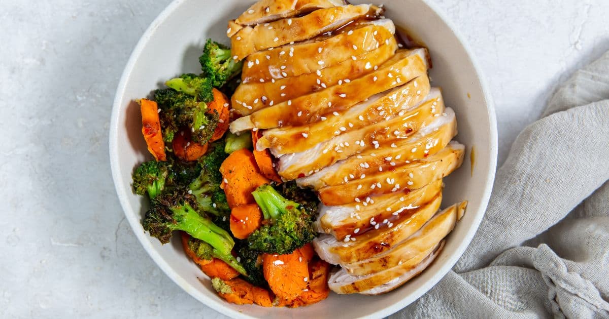 Easy Air Fryer Teriyaki Chicken Breast in a white bowl with sesame seeds, carrots, and broccoli.