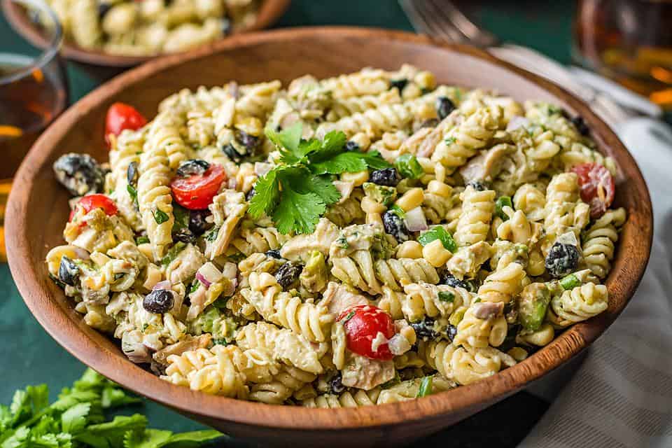 A pasta salad in a large wood bowl on a table. 