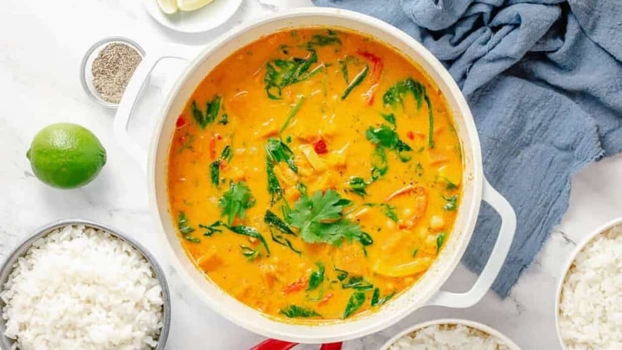 Thai pumpkin curry in a white dutch oven with rice and limes on the side.