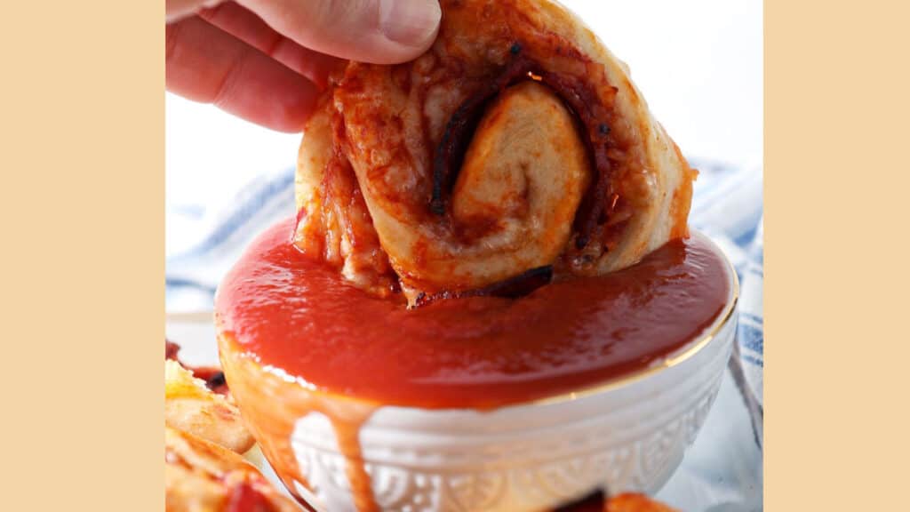 Pepperoni pinwheels being dipped in pizza sauce.