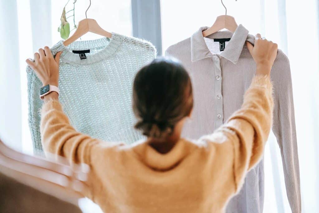 A woman holding up two pieces of clothing at a store.