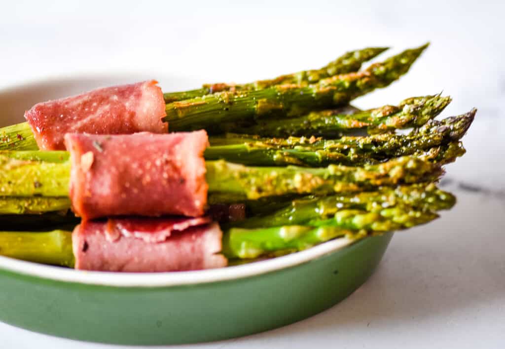 Closeup side view shot of turkey bacon wrapped asparagus bundles in a green dish.