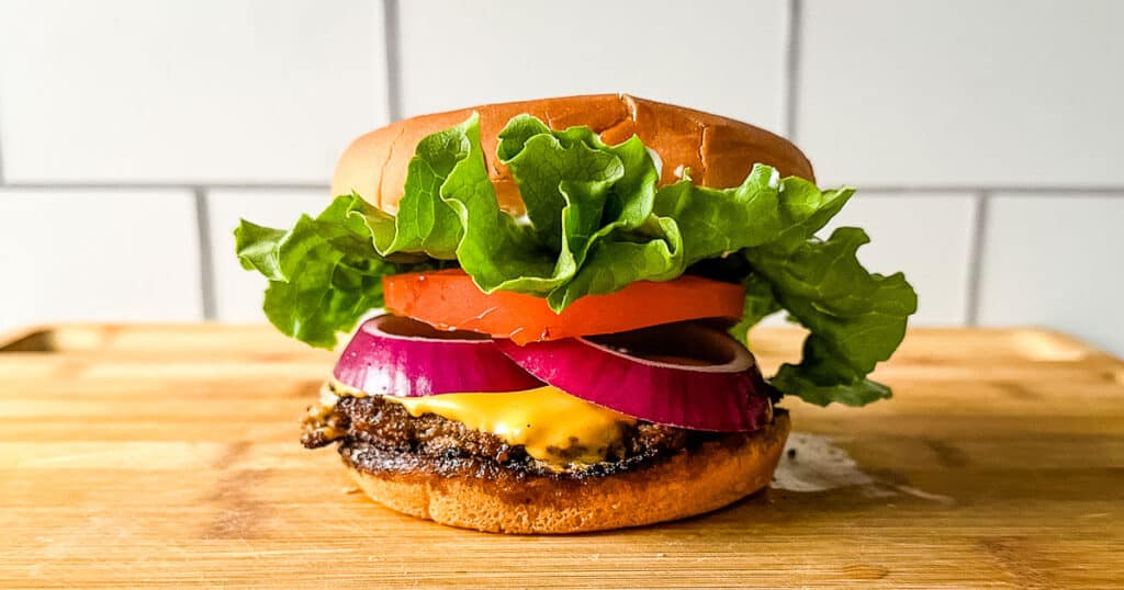 Turkey smash burger topped with onions, tomato, and lettuce on a wooden cutting board.