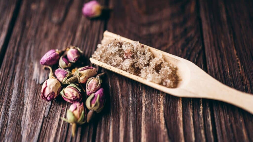 A wooden spoon filled with sugar and rose petals.