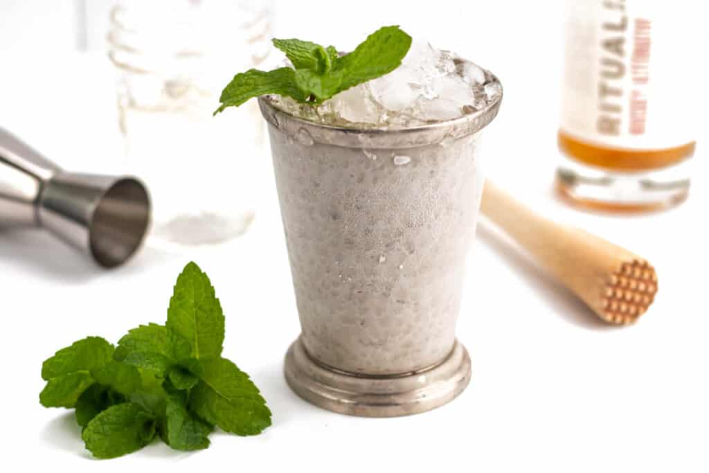 a mint leaf on top of a mint julep next to a bottle of zero-proof whiskey.