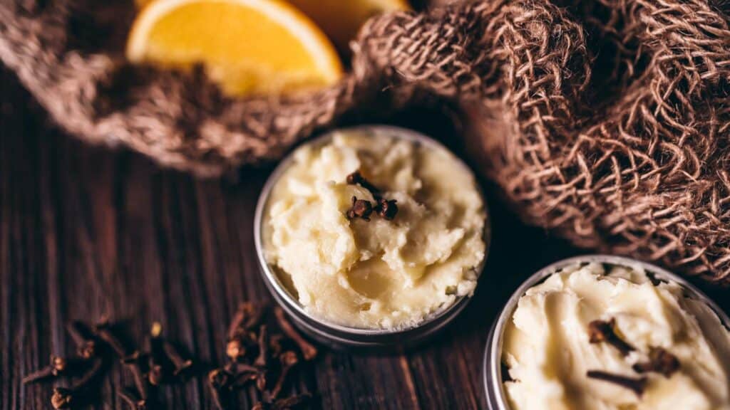 Small tins of homemade body butter topped with cloves and orange slices.