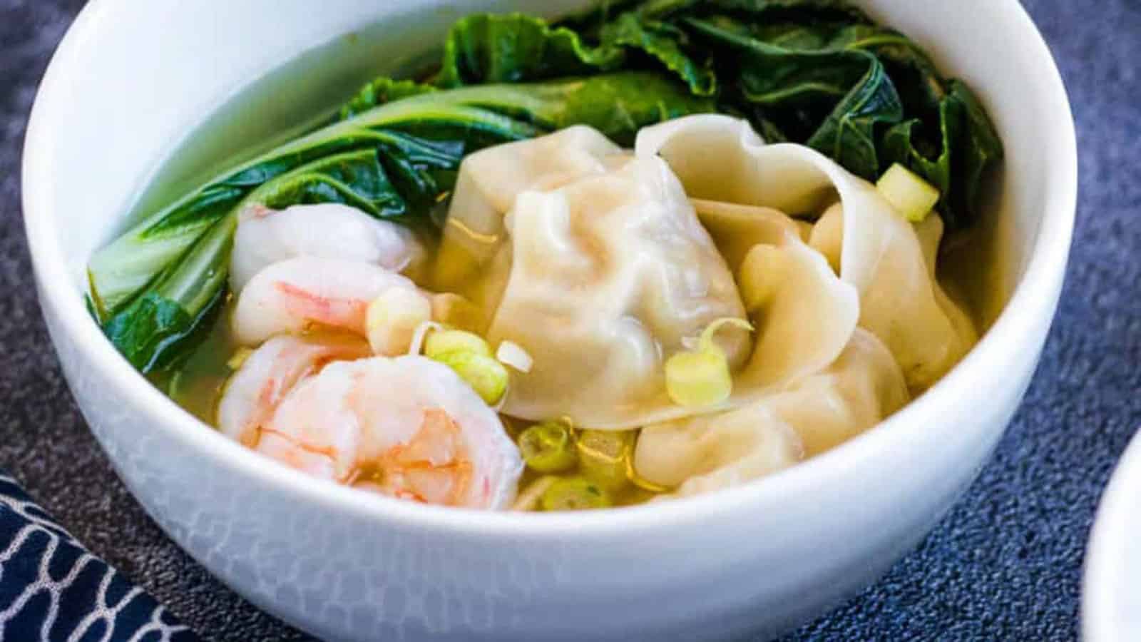 wonton soup with shrimp in a white bowl.