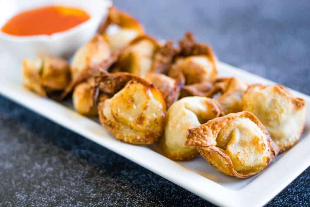 Air fryer wontons on a plate with dipping sauce.