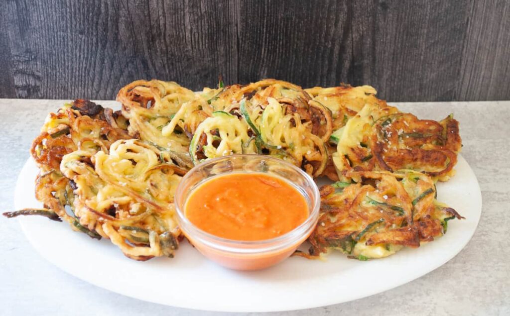 Zucchini fritters on a platter with a dipping sauce in a small bowl.