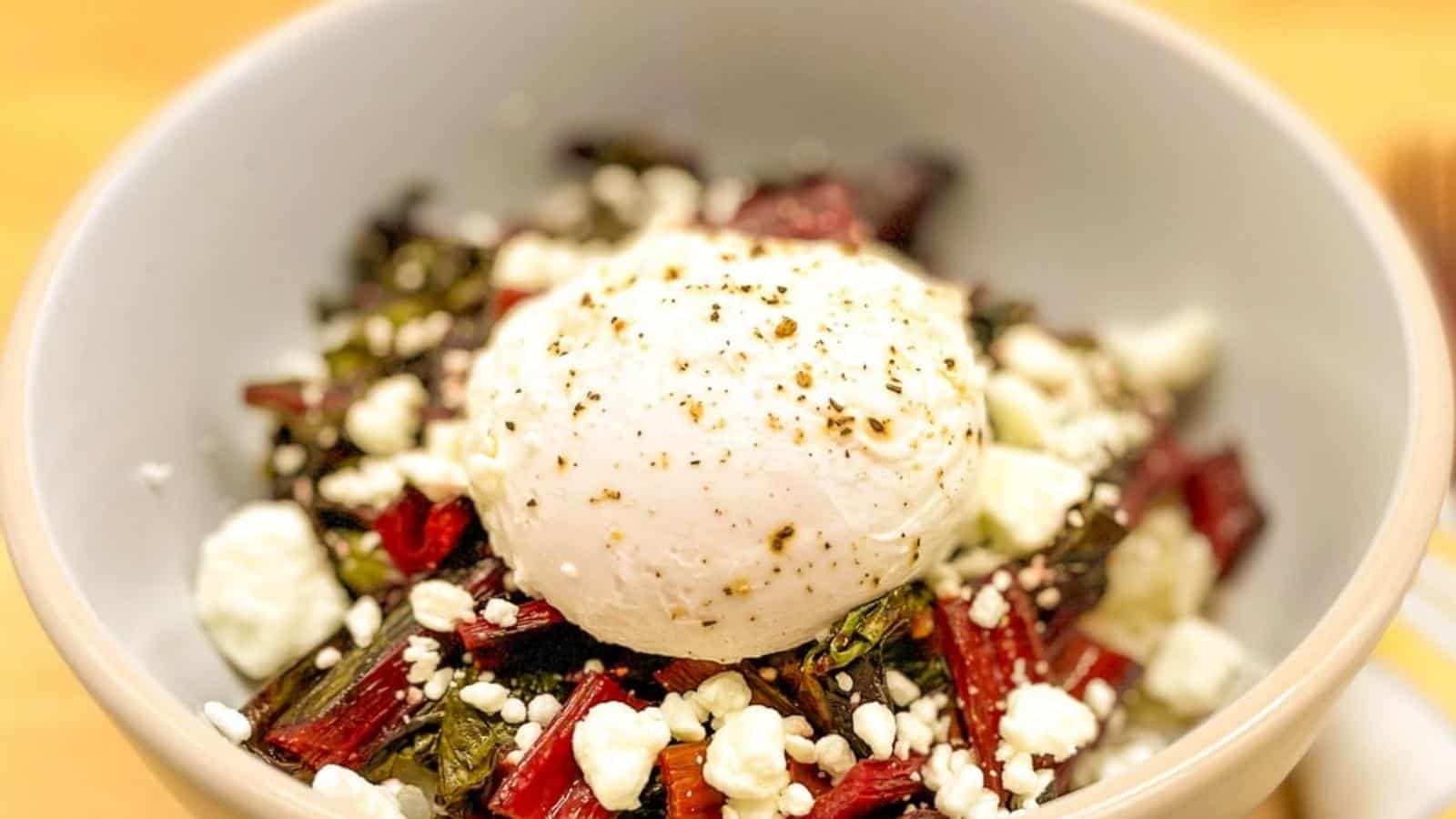 Grain bowl topped with sauteed swiss chard, goat cheese, and a poached egg.