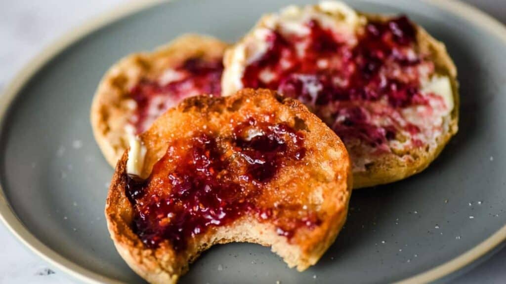 Air fryer english muffins on a blue plate topped with butter and jam.
