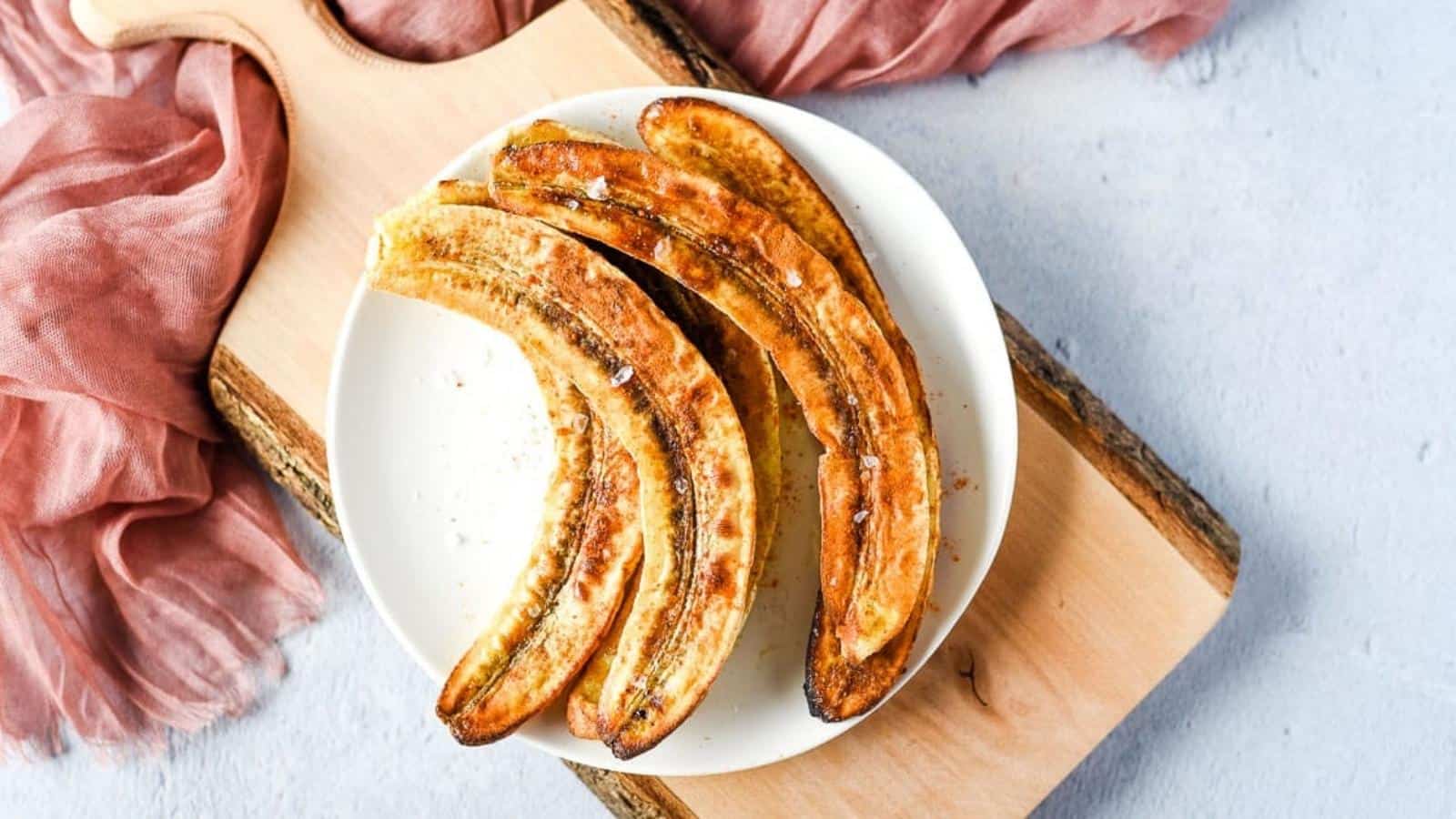 Air fryer bananas on a white plate over a rustic wooden cutting board with a pink linen.