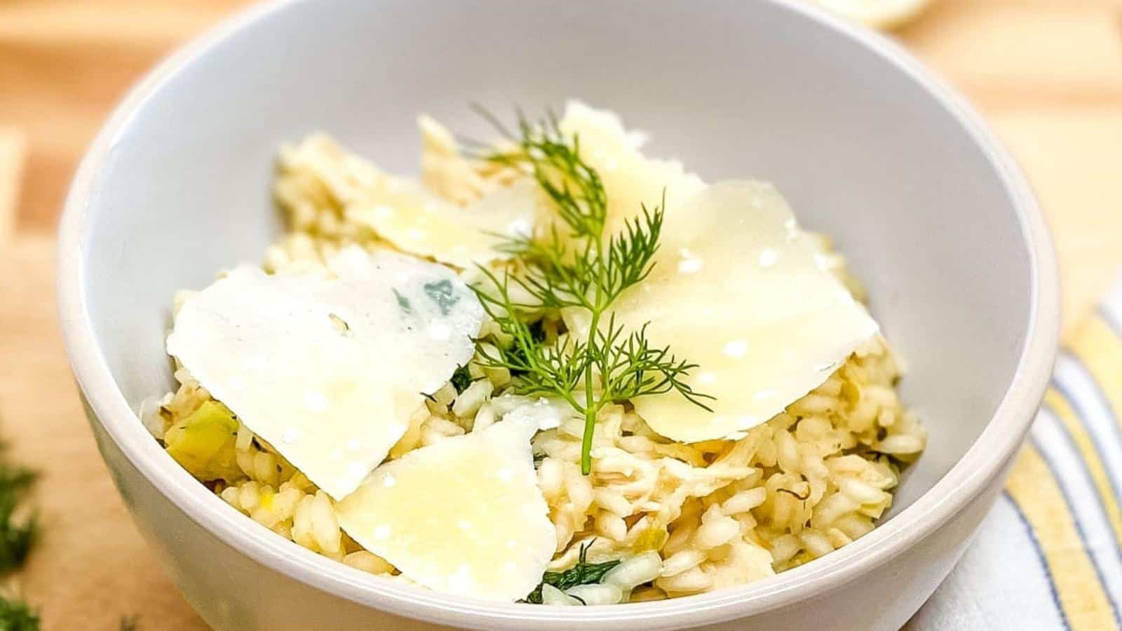 Chicken and leek risotto topped with parmesan and fresh dill in a white bowl.
