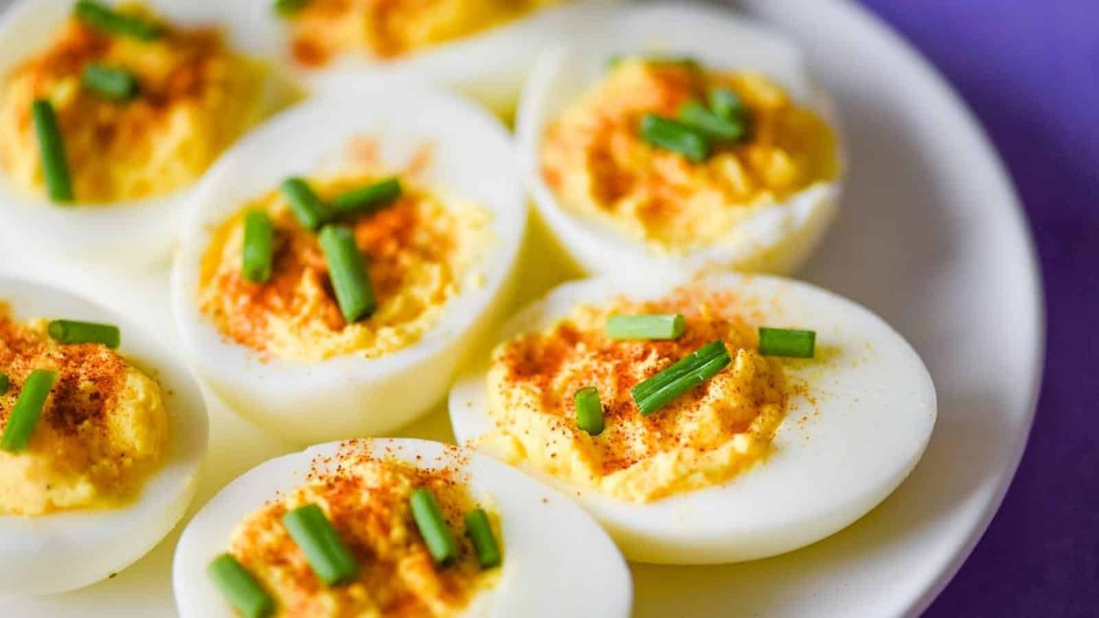 closeup shot of deviled eggs without mustard topped with snipped chives and paprika on a white plate.