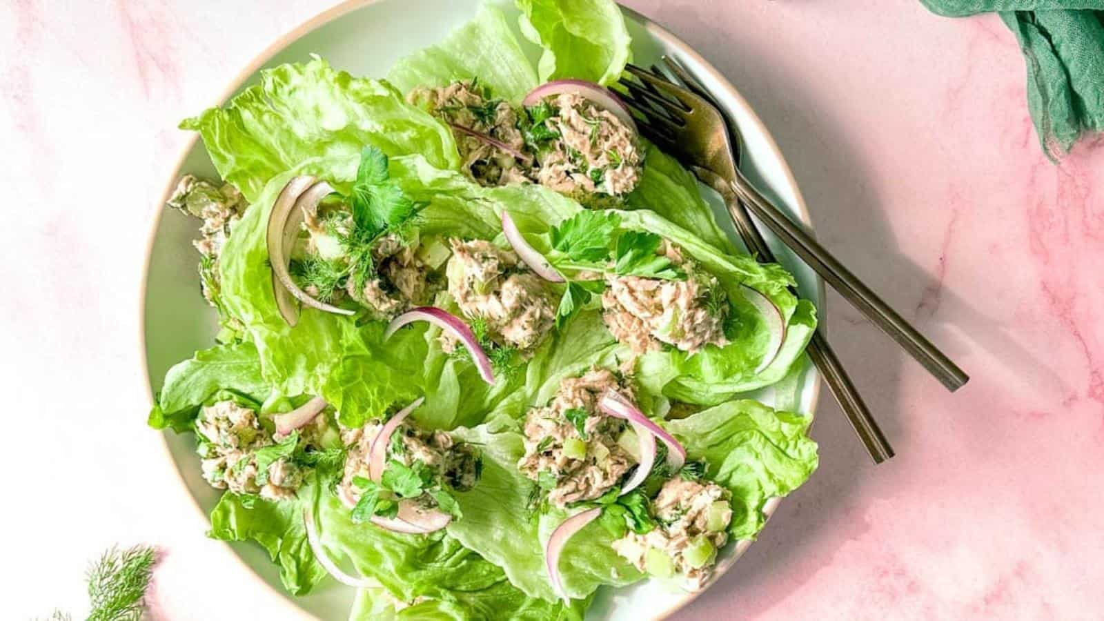Healthy Tuna salad without mayo sits on a bed of iceberg lettuce surrounded by two forks, dill, and a green linen.
