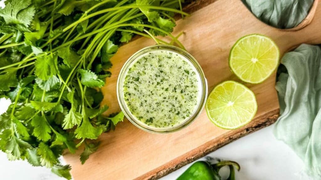 Honey lime jalapeno vinaigrette on a wooden cutting board surrounded by cilantro and limes.