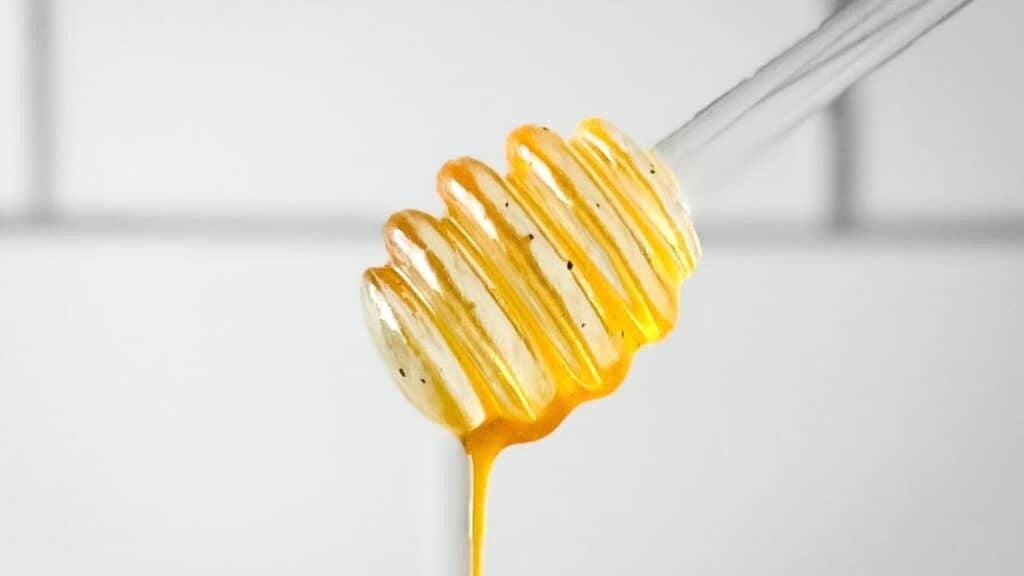 Hot honey sauce drips from a honey dipper.